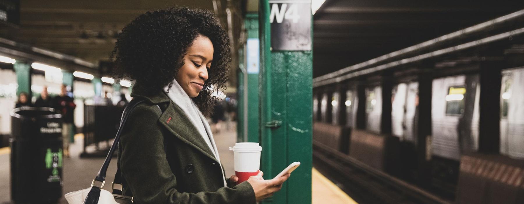 woman with a cup of coffee texts on subway station platform