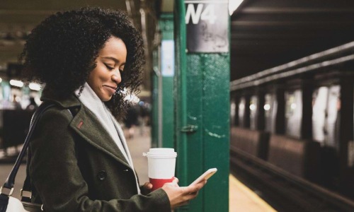 woman with a cup of coffee texts on subway station platform